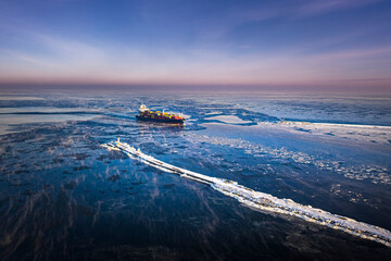 Cargo ship driving through frozen sea with colorful containers. Dark waters with ice blocks...