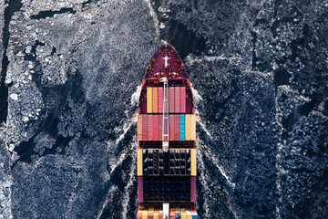 Cargo ship driving through frozen sea with colorful containers. Dark waters with ice blocks...