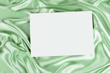 Mock up blank white board canvas poster card for text greeting over draped green color silk cloth background. Top view