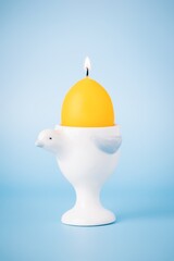Yellow easter burning egg candle in egg cup on a light blue background, copy space