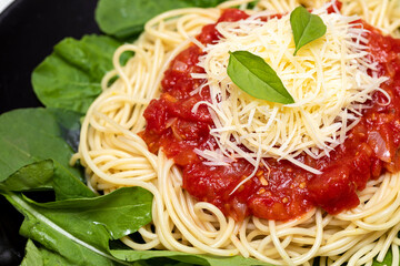 Spaghetti pasta with red sauce, arugula and parmesan cheese on black plate with white marble background