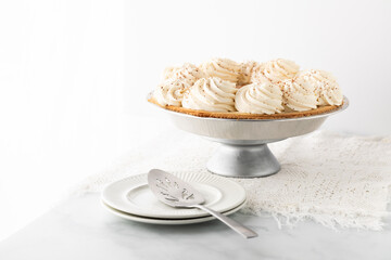 A unsliced whole banana cream pie against a brightly lit window.