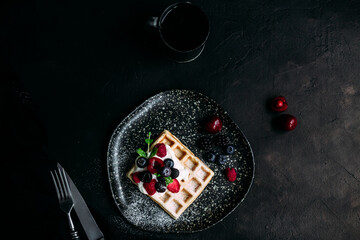 Belgian waffles with wild berries and cream cheese on a dark background