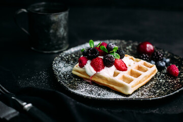 Belgian waffles with wild berries and cream cheese on a dark background