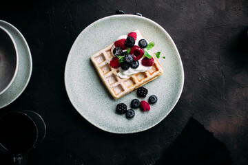 Belgian waffles with wild berries and cream cheese on a dark background