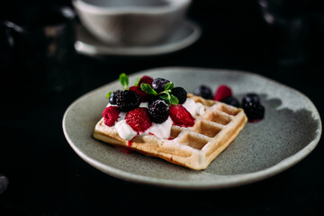 Belgian waffles with wild berries and cream cheese on a dark background