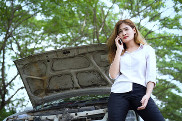 Beautiful woman with broken car on the road waiting to get help. Repairing in the bright sunlight.