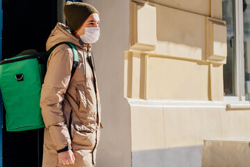 Caucasian delivery man wearing warm clothes with green delivery backpack smilly happy outdoors in winter cold day city street.