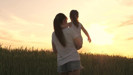 Mom and daughter walk past a wheat field and admire the sun's rays. Happy family mom and daughter in field at sunset. Mother farmer and child. The concept of happy family and being with nature