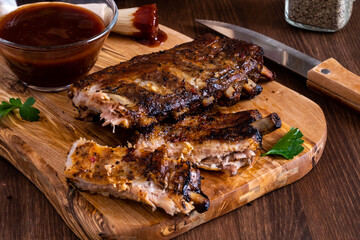 Close up of spareribs on a wooden board with barbecue sauce in behind.