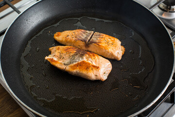pieces of salmon cooking on a hot pan with olive oil on a gas stove.