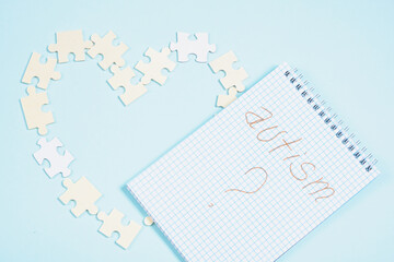 notepad with the inscription autism and wooden puzzle pieces are laid out in the shape of a heart on a light blue background copy space