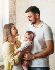 Young beautiful parents man and woman with baby daughter in arms look at each other