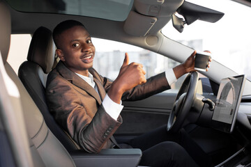 Cheerful smiling African man businessman, sitting in his new high tech electric car with upgraded...