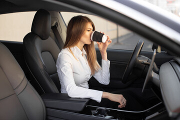 young pretty businesswoman drinking take away coffee, sitting inside of autonomous driverless electric car. self-driving vehicle. automotive technology.