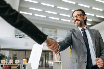 Successful grey-haired male leader of the company is shaking hands with business partner on meeting. Influential colleagues coming to agreement on negotiations, sign corporate contract