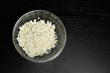 Grained cottage cheese in a glass bowl on a black background close-up copy space, top view