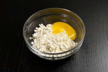 Grainy cottage cheese, egg in a glass bowl on a black table close-up