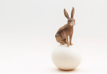 The Easter bunny toy sits on a chicken egg. A small toy rabbit is isolated on a white background. Minimal Easter Concept. Copy space. Mock up