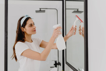 Fototapeta na wymiar Beautiful woman cleaning mirror in bathroom at home.