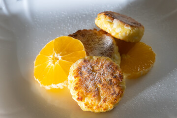 Sweet cottage cheese pancake sprinkled with powdered sugar with orange close-up on a white plate. Concept of a delicious, healthy breakfast