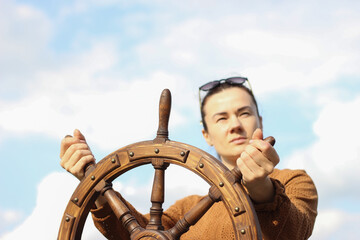 The girl controls the yacht, hands on the steering wheel,  handwheel on sky background