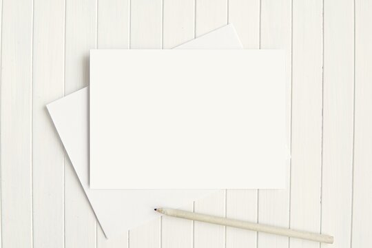Blank horizontal greeting card mockup for stationery, invitation or thank you card design presentation with envelope and pencil, white wooden background.