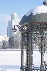 Winter view of the rotunda made of black cast iron on the shore of the city pond