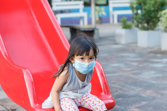 Portrait image of 2-3 yeas old baby. Happy Asian child girl smiling and wearing fabric mask,​ She playing with slider bar toy at the playground, social​ Distance,​ Learning and active of kids concept.