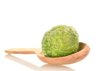 One frozen organic Brussels sprouts with a spoon made of wood, close-up, isolated on white.