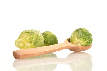 Several frozen organic Brussels sprouts with a spoon made of wood, close-up, isolated on white.