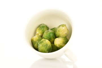Several frozen organic Brussels sprouts in a ceramic bowl, close-up, isolated on white.