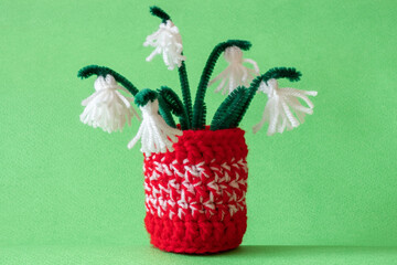 Close up red and white yarn strains of crochet vase and tassel snowdrops flowers as martenitsa, Bulgarian folklore tradition in march, Baba Marta day. Shallow depth of focus. Light green background.
