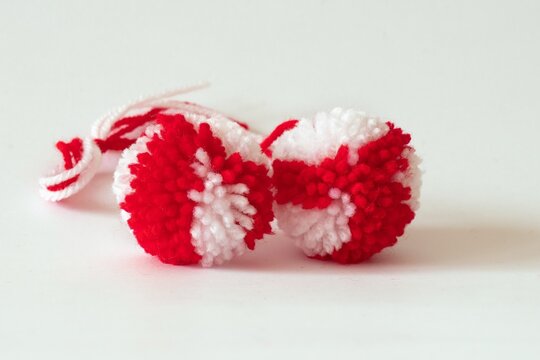 Close up red and white pompoms as martenitsa - bulgarian folklore tradition in March Baba Marta day. Shallow depth of focus, colorful yarn strains in two balls, light background.