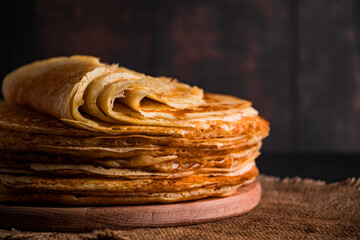 Traditional Russian food - thin pancakes. A stack of crepes on a dark brown wooden background. Rustic style.