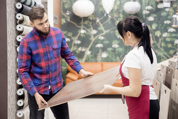 Woman consultant shows laminate flooring to a man in a store