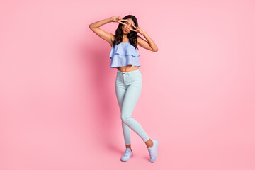 Fototapeta na wymiar Full size photo of optimistic brunette lady show v-sign blow kiss wear blue top trousers sneakers isolated on pink color background