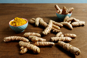 Turmeric unpeeled root and powder in blue bowls  at brown table.