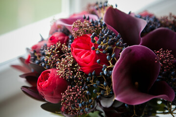 a beautiful and expensive bouquet with red roses and purple calla lilies and dark blue berries. bouquet in the color of wine and marsala