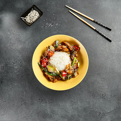 Sweet and Sour Chicken and Vegetables with Rice. Stir Fry Chicken with Vegetables and Sesame. Yellow plate with wooden chopstick on dark slate table. Chinese, asian, authentic food concept
