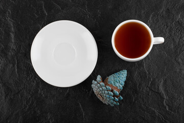 A white cup of hot tea with a Christmas pinecone