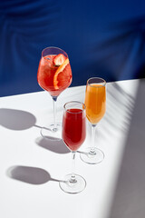 Aperol drink and bellini cocktail on white table with blue background. Sunshine and palm leaf shadow drink modern still life. Summer, party, tropical and freshness concept