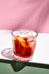 Negroni cocktail over pink background. Drink in rox glass in daylight with palm leaf hard shadow. Summer, tropical, fresh drink concept