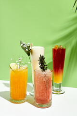 Various lemonade drink over green background. White table with sunlight and palm leaf hard shadow. Summer, tropical and juicy concept