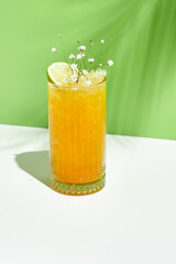 Mango lemonade drink over green background. White table with sunlight and palm leaf hard shadow. Summer, tropical and juicy concept