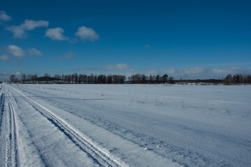 Obraz premium Landscape of a winter road on a completely snowy white field under a blue sky with sparse clouds on a sunny frosty day.