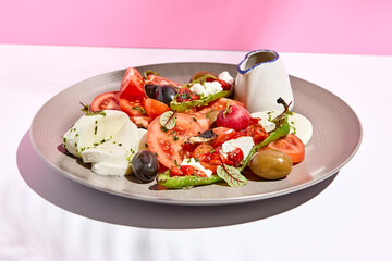 Tomato, olives and mozzarella salad . Restaurant appetizer plate on white table with pink wall. Day sunlight with hard shadow of fern palm leaves. Summer or spring restaurant food concept