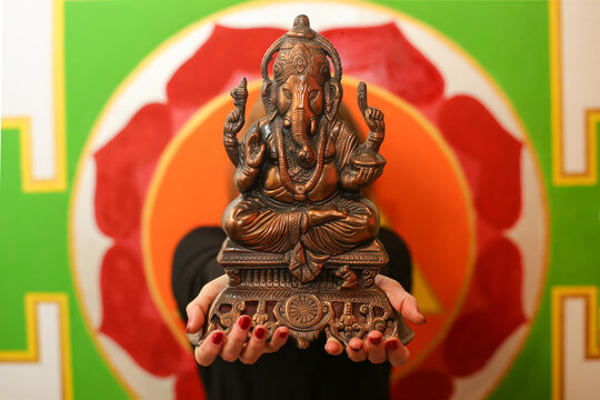 A statue of an Indian god, Lord Ganesha in female hands on the background of a wall with a mandala