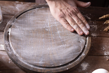 Baker male hand scattering flour for kneading dough at wooden pizza board