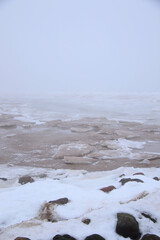foggy beach with rocks in snow and ice at winter